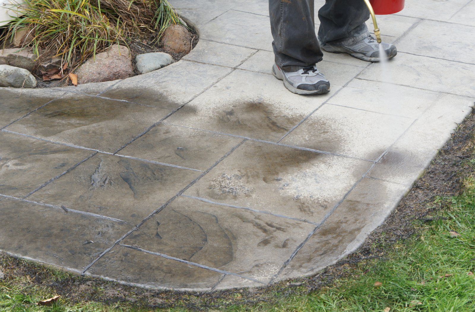 Concrete worker spraying stain onto a stamped concrete patio.