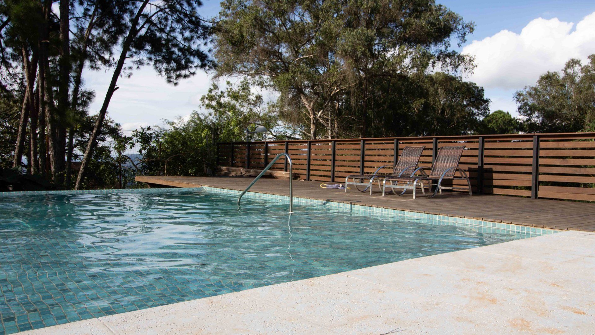 Picture of a pool surrounded by a wooden fence and concrete pool deck.