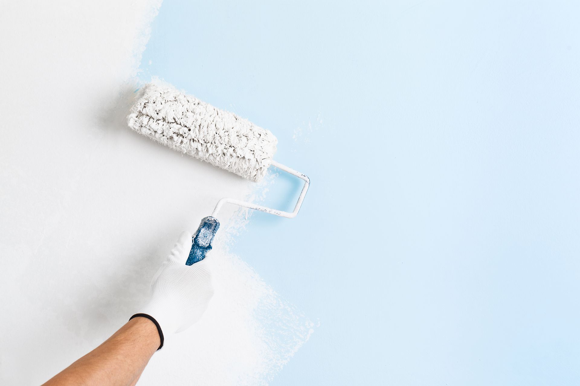 a person is painting a light blue wall with a white paint roller