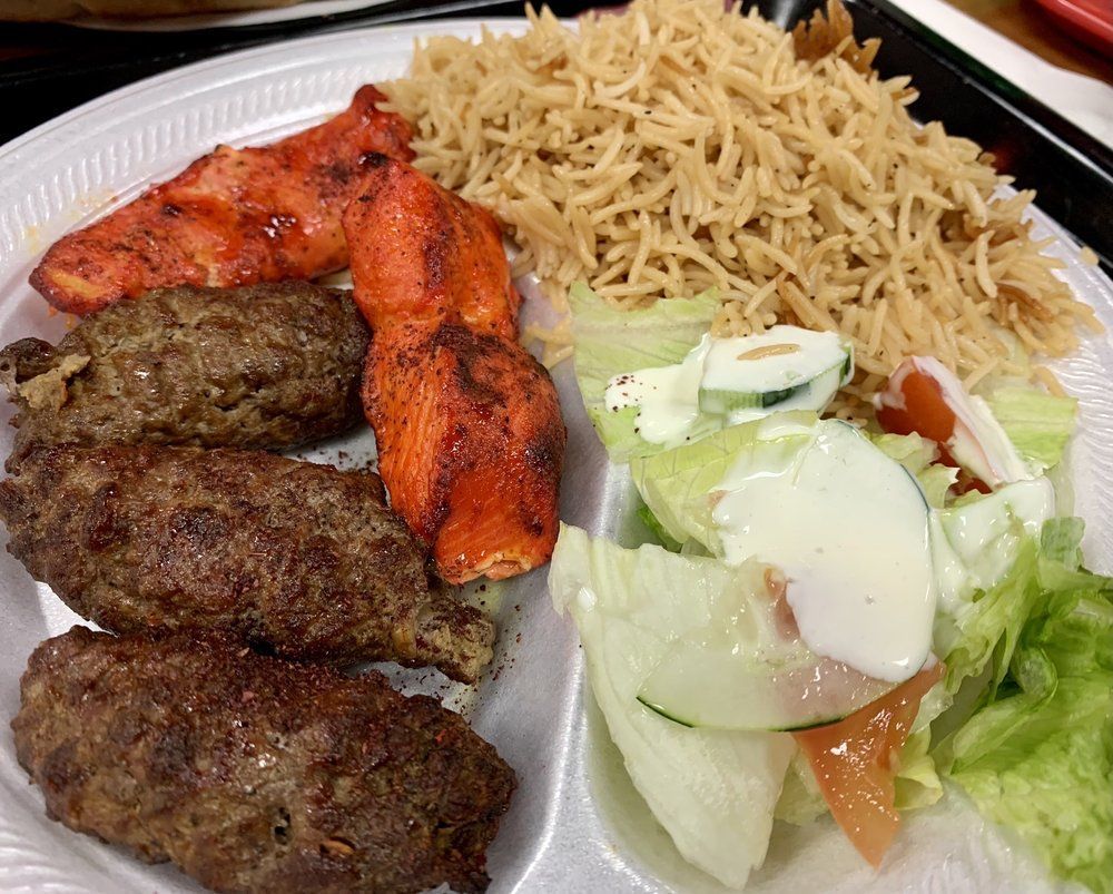 A plate of food with rice , meat , vegetables and bread on a table.