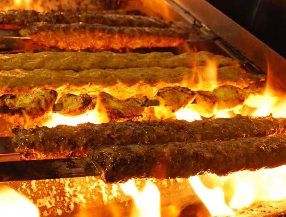 A bunch of kebabs are cooking on a grill with flames.