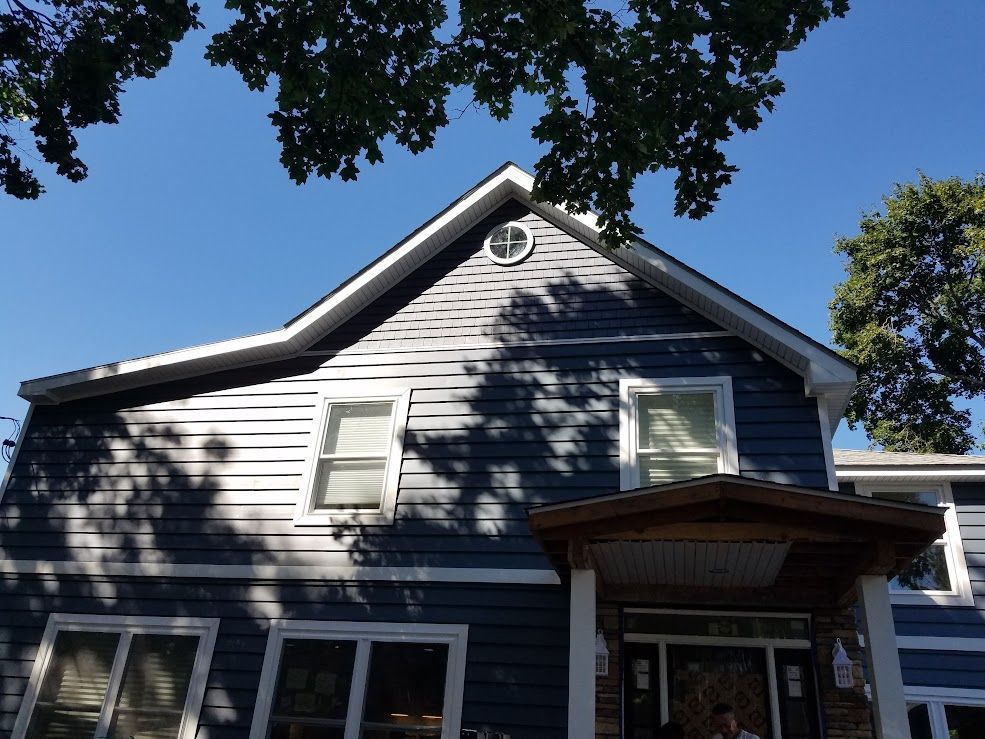 Blue two-story house with white trim, blue siding, and a round window in the peak; clear blue sky.