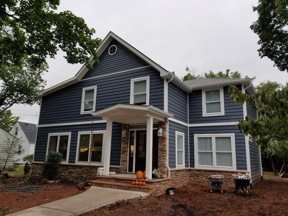Two-story house with blue siding, stone accents, and white trim. A porch with a pumpkin is in front.