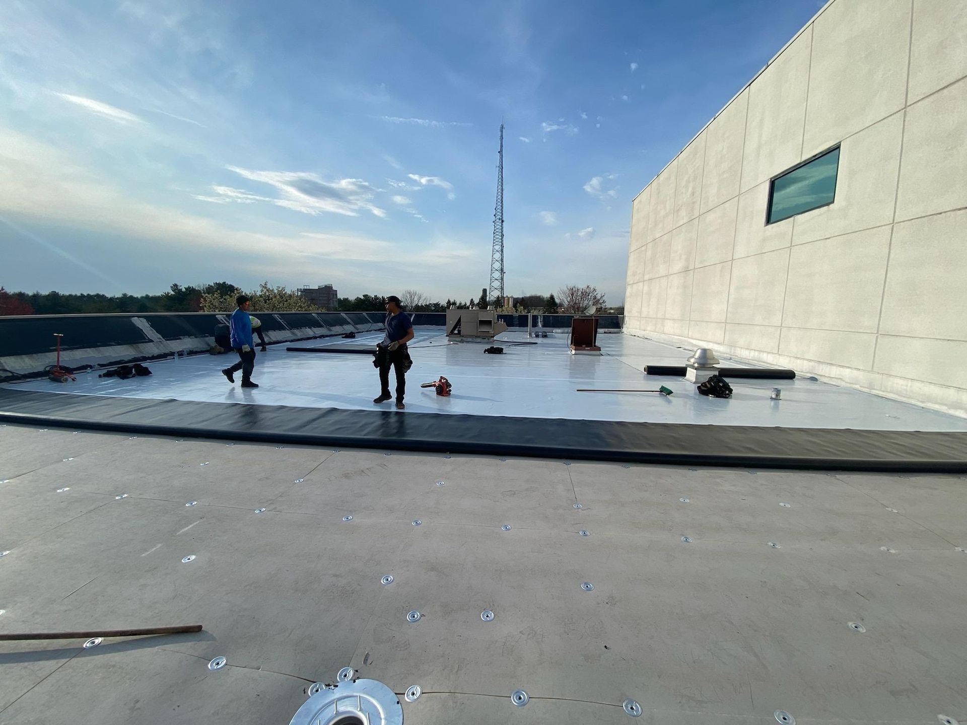 Two people on a flat rooftop with construction materials. A light blue sky is overhead.