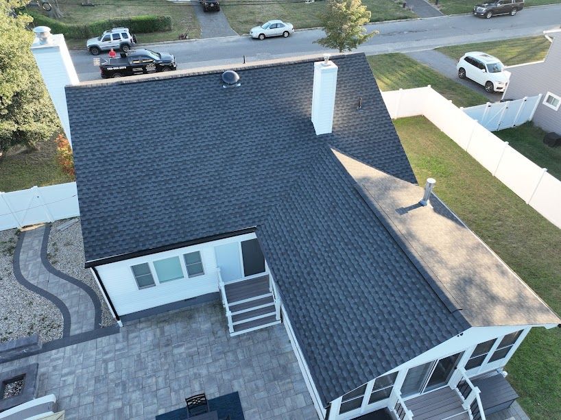 Aerial view of a white house with a dark gray roof, chimney, and patio.