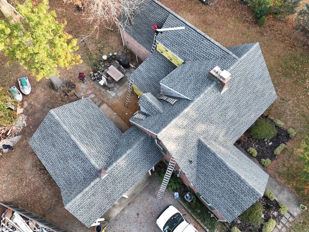 Aerial view of a house with newly shingled gray roof and partially yellow underlayment.