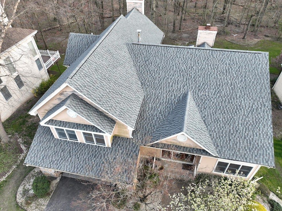 Overhead view of a house with a gray roof, brown exterior, and a driveway leading to a garage.