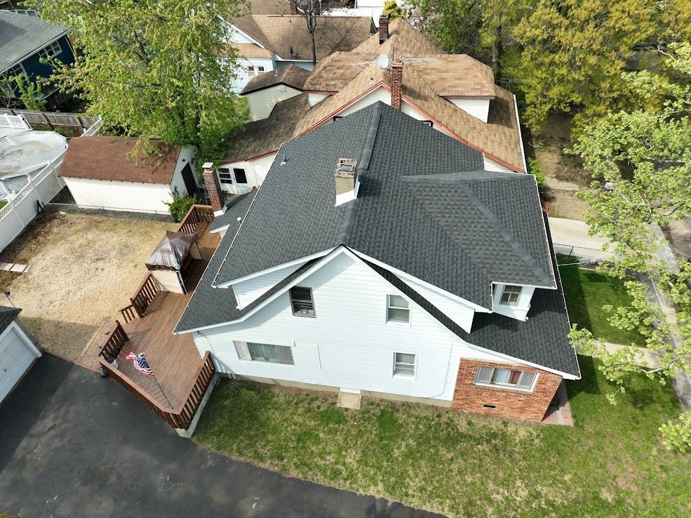 Aerial view of a two-story white house with a black roof and a brick facade, surrounded by other houses and trees.