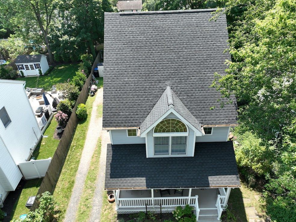 Overhead view of a gray house with a black roof, a white porch, and a driveway next to a fence.