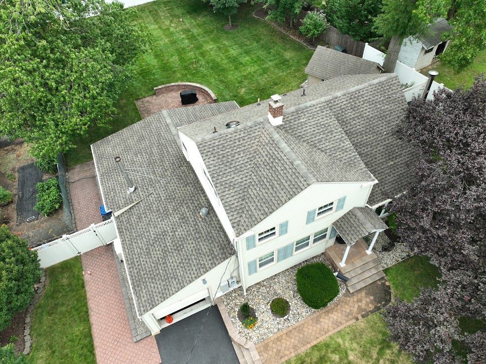 Overhead view of a two-story house with a gray roof, surrounded by a lawn and trees.