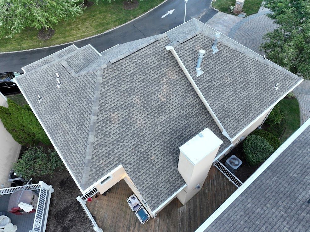 Overhead view of a house roof with gray shingles, white trim, and chimneys.