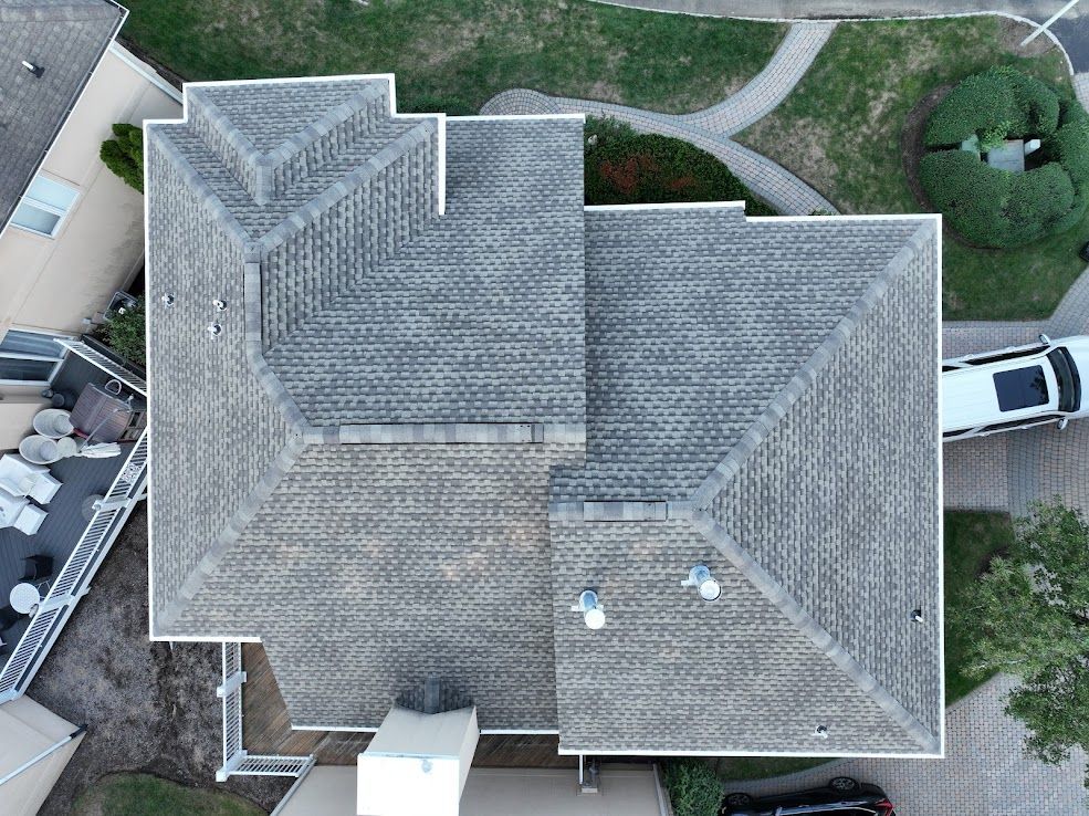 Overhead view of a house with a gray shingle roof, surrounded by lawn and a driveway with cars.