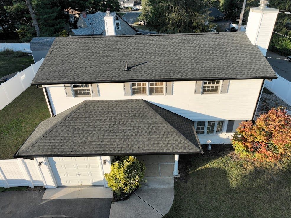 Overhead view of a two-story white house with a dark gray roof and black trim, surrounded by a white fence and green lawn.