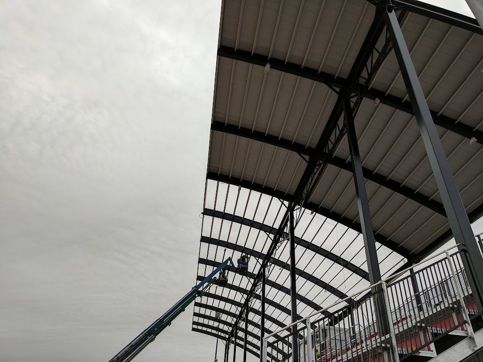 Person on lift working on curved metal roof structure under overcast sky.