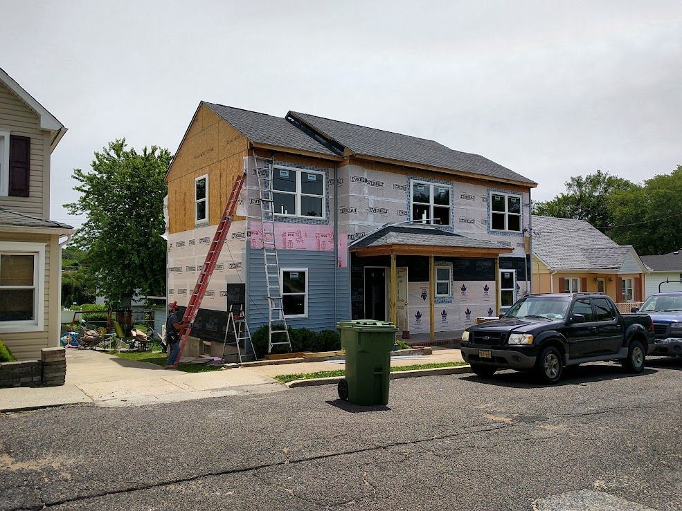 House under construction, wood and siding partially installed, with a ladder and a trash can on the street.