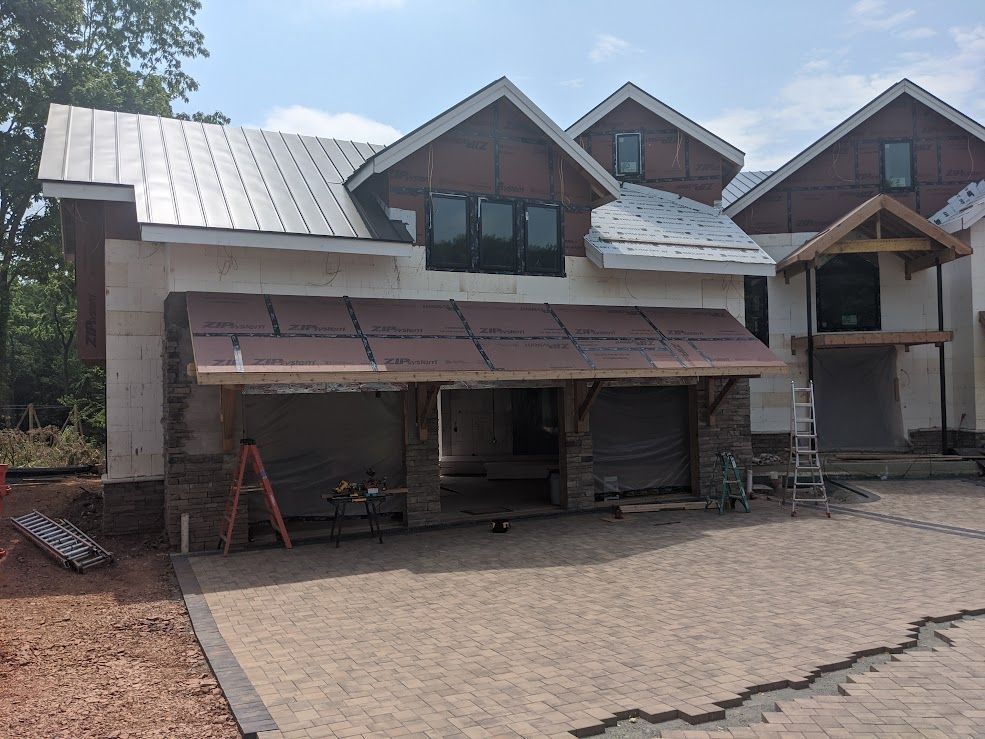 Building under construction; tan siding, brown roof, stone facade, and gray pavers.