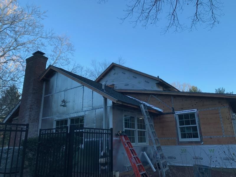 House under construction, with new sheathing and roof, chimney, ladder, and a blue sky.
