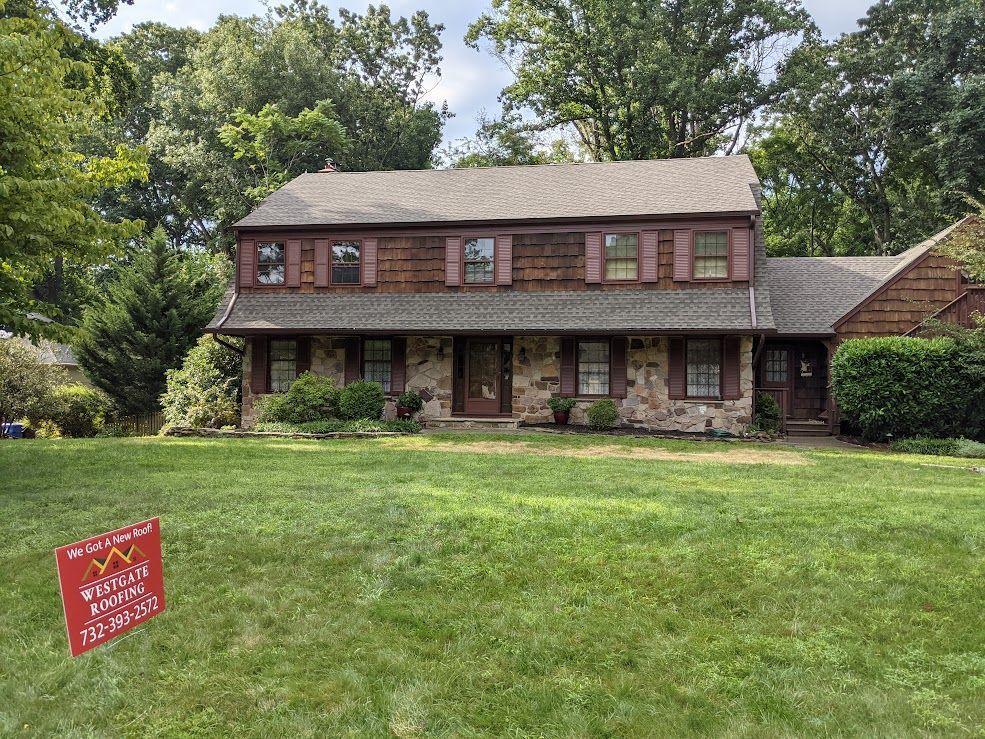 Two-story house with stone and wood siding, shutters, and a lawn. A sign is in the front yard.