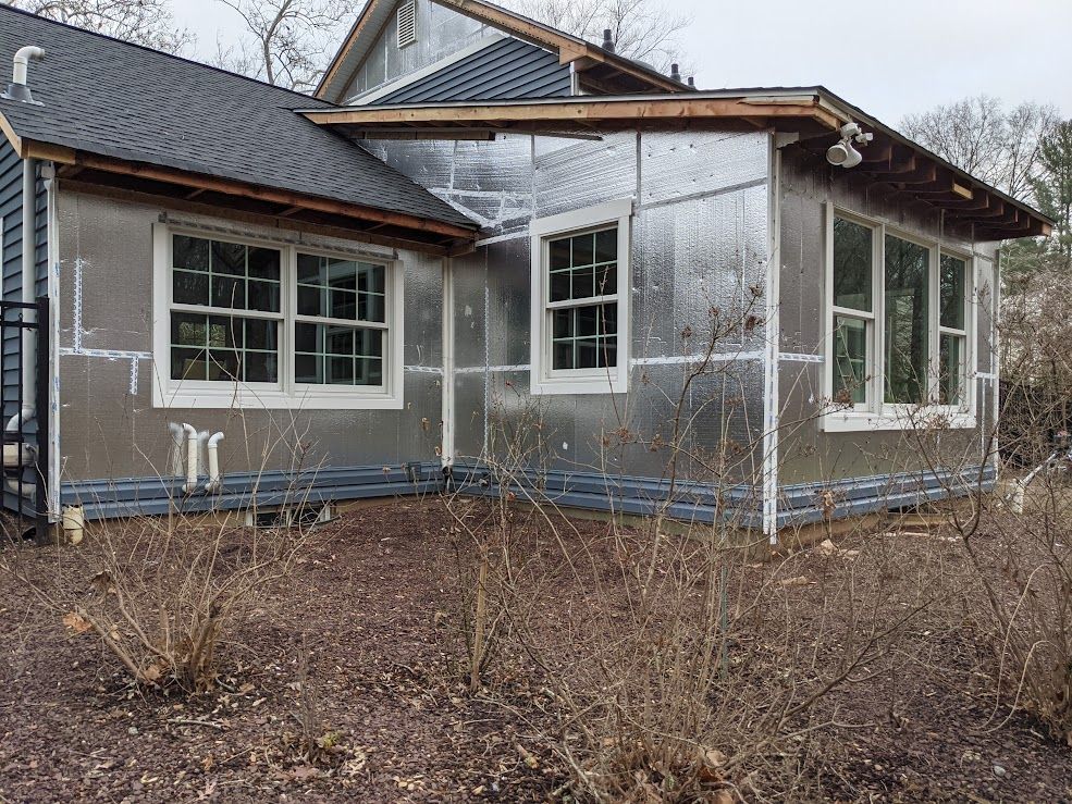 House exterior under construction, silver insulation visible. Windows and dark roof.