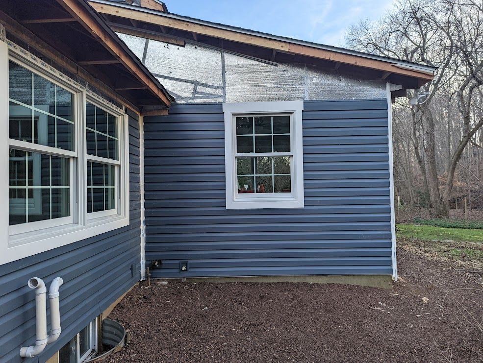 Exterior house with blue siding, a white-framed window, and unfinished section with insulation.