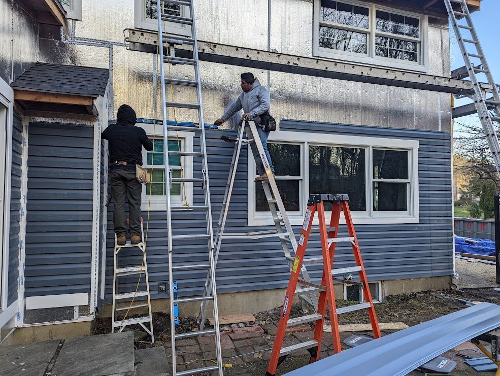 Two workers installing blue siding on a house exterior using ladders.