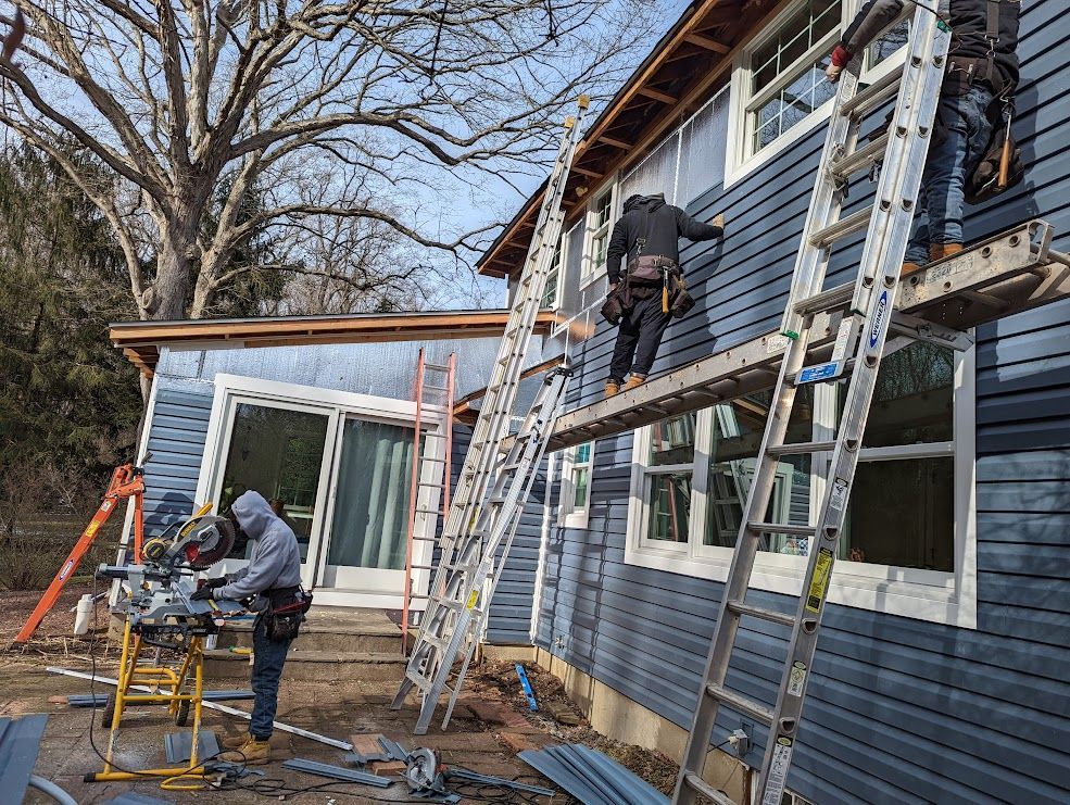 Construction workers siding a blue house, using ladders, saws, and a platform.
