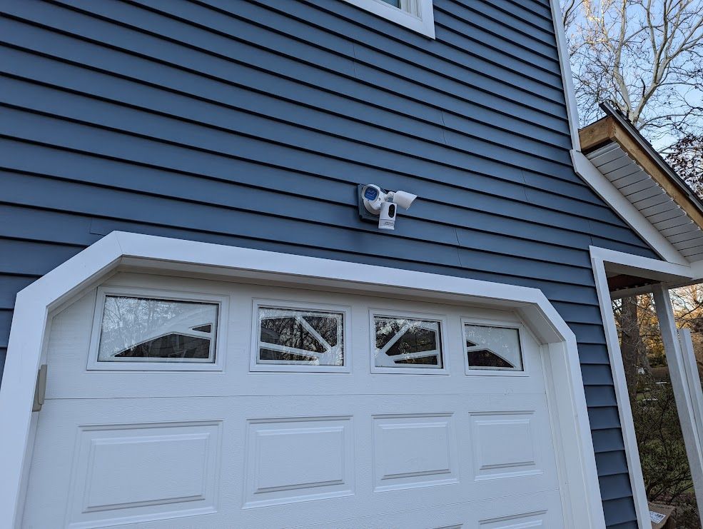 Blue siding, white garage door with windows, security light on exterior wall.