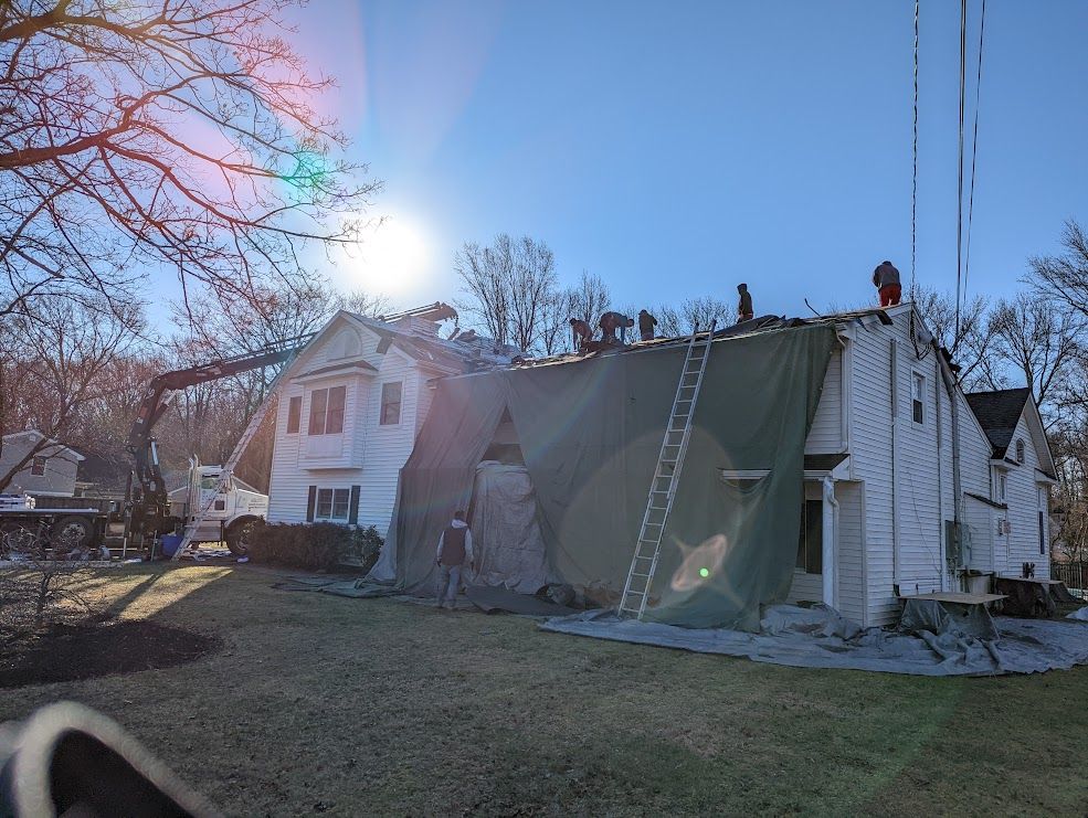 Roofers on a house under construction; green tarp covers the structure, sunny day.