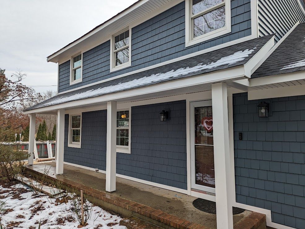 Blue-sided house with white trim, porch, and a snowy landscape.