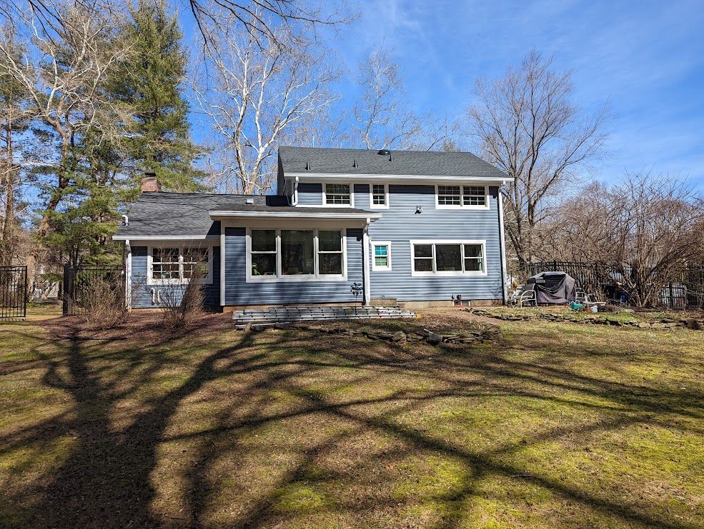 Back view of blue house with several windows, surrounded by trees and a grassy yard.