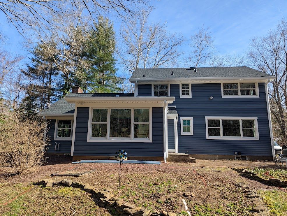 Blue two-story house with white trim. Windows on the first and second floors, surrounded by trees and brush.