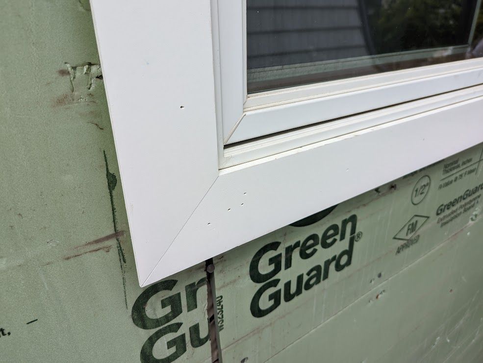 White window frame on green house wrap.