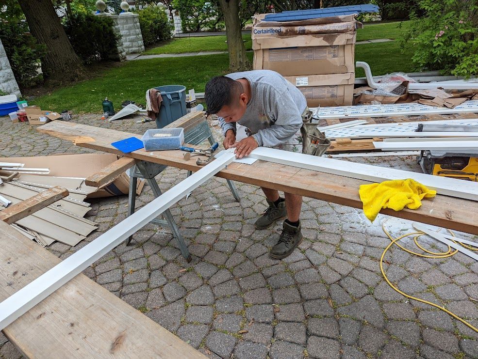 Person cuts white trim on wooden planks outdoors.