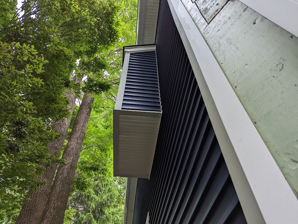 Side view of a building with dark blue siding, a white trim, and a small, gray overhang.