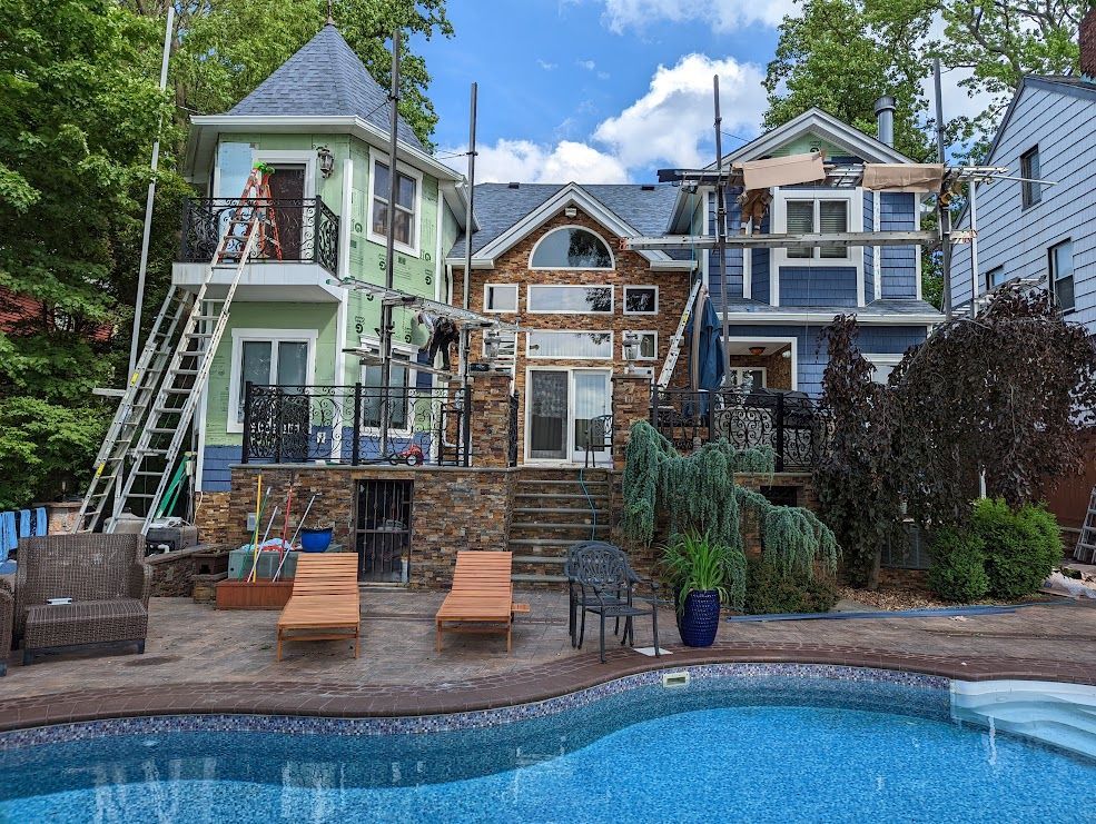 A multi-colored house under construction, with a pool in the foreground. Scaffolding is set up around the roof.