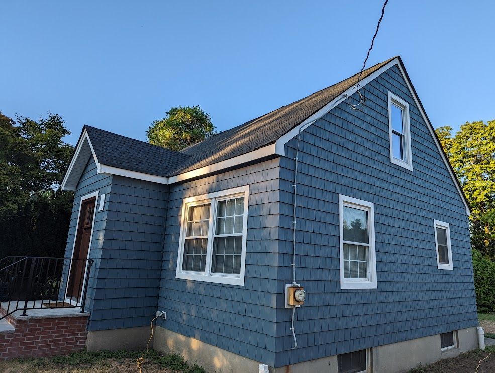 Blue-sided house with a dark roof and white-framed windows against a blue sky.