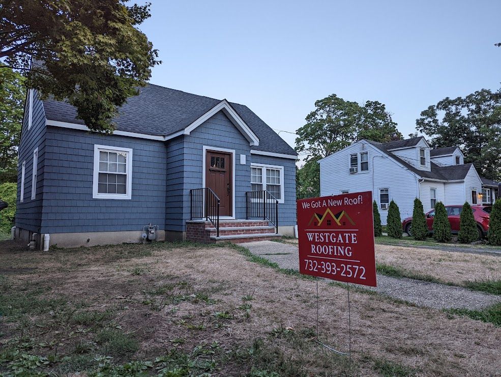 Blue house with roofing sign, grass in foreground, houses in background.