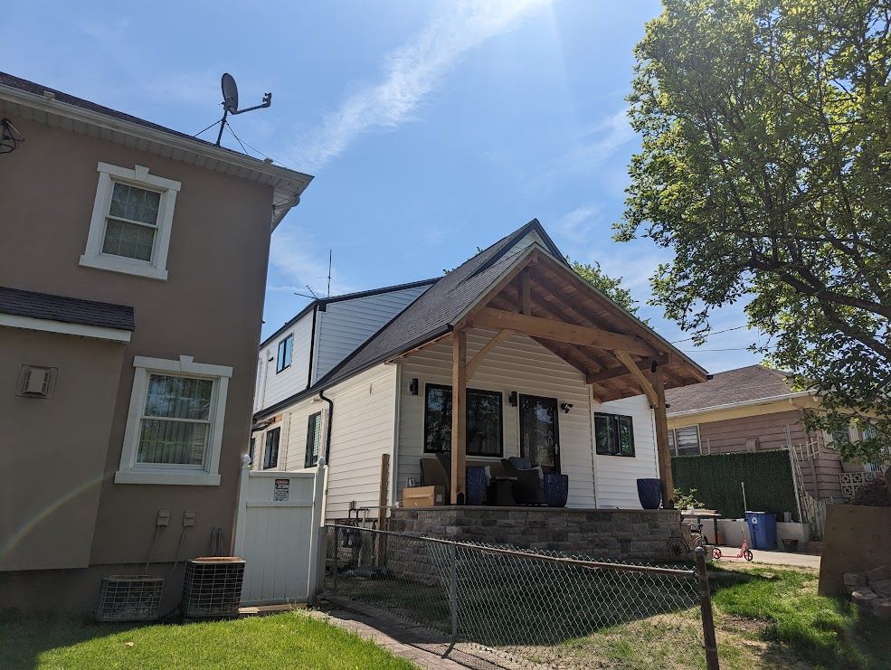 Backyard with white and brown buildings, wooden porch, blue sky, and green grass.