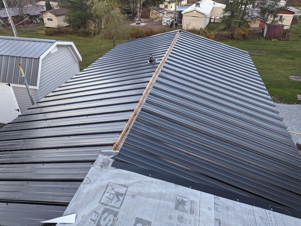 Newly installed metal roofing on a house, angled view. Gray metal, wood frame, and nearby buildings.