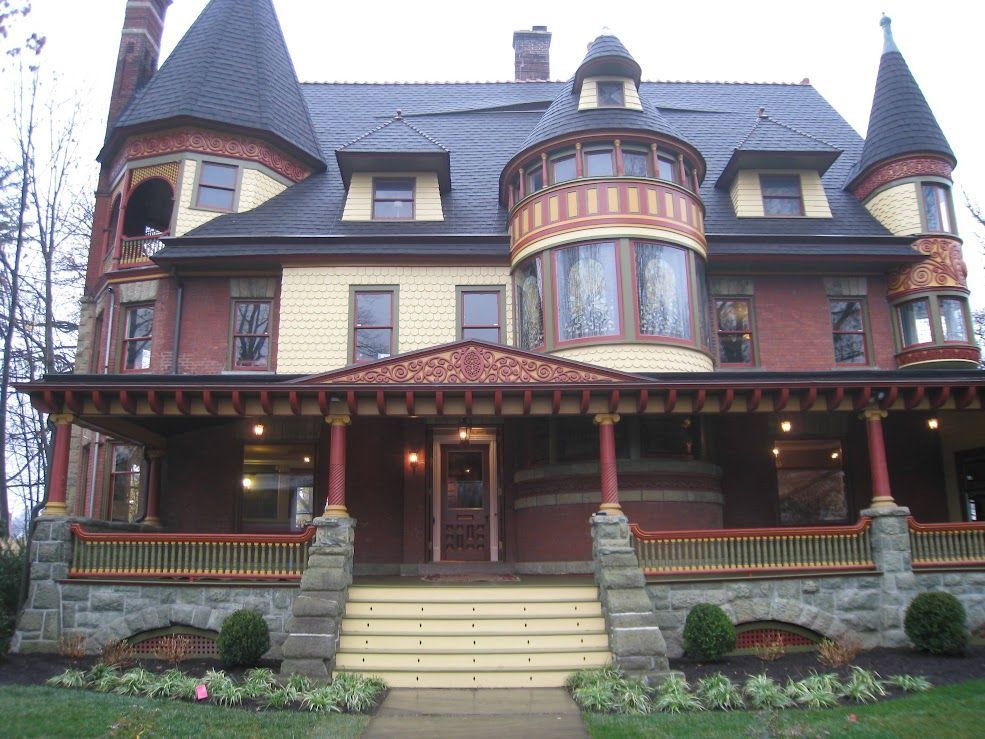 Victorian mansion with red brick, yellow siding, and decorative porch.
