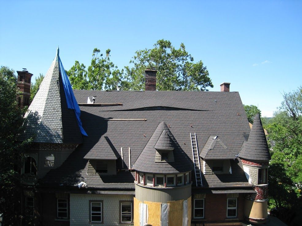 House with damaged roof, blue tarp, multiple turrets, and a ladder.