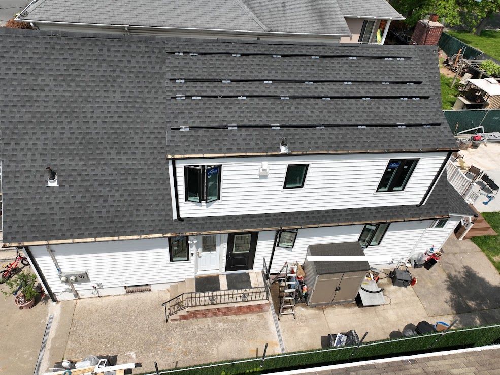 Two-story white house with solar panels on dark gray roof; back patio, some construction equipment present.