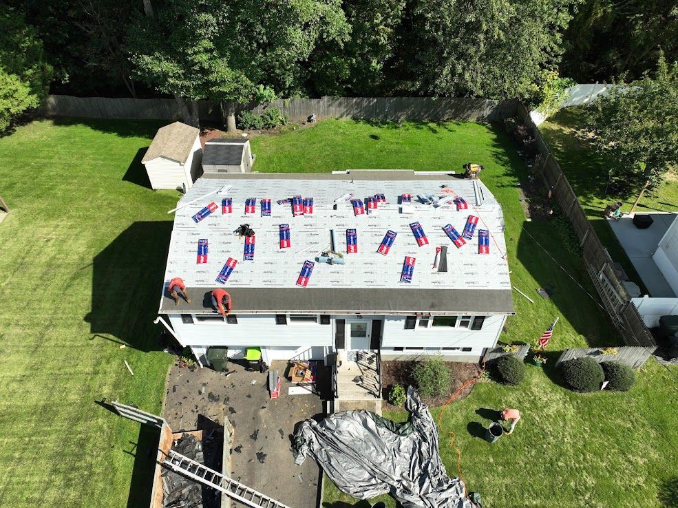 Roofers replacing a house roof; workers on the roof, material spread across surface, green lawn, sunny day.