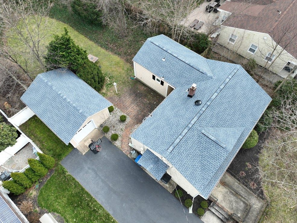 Aerial view of a house and detached garage with gray roofs and a long driveway.