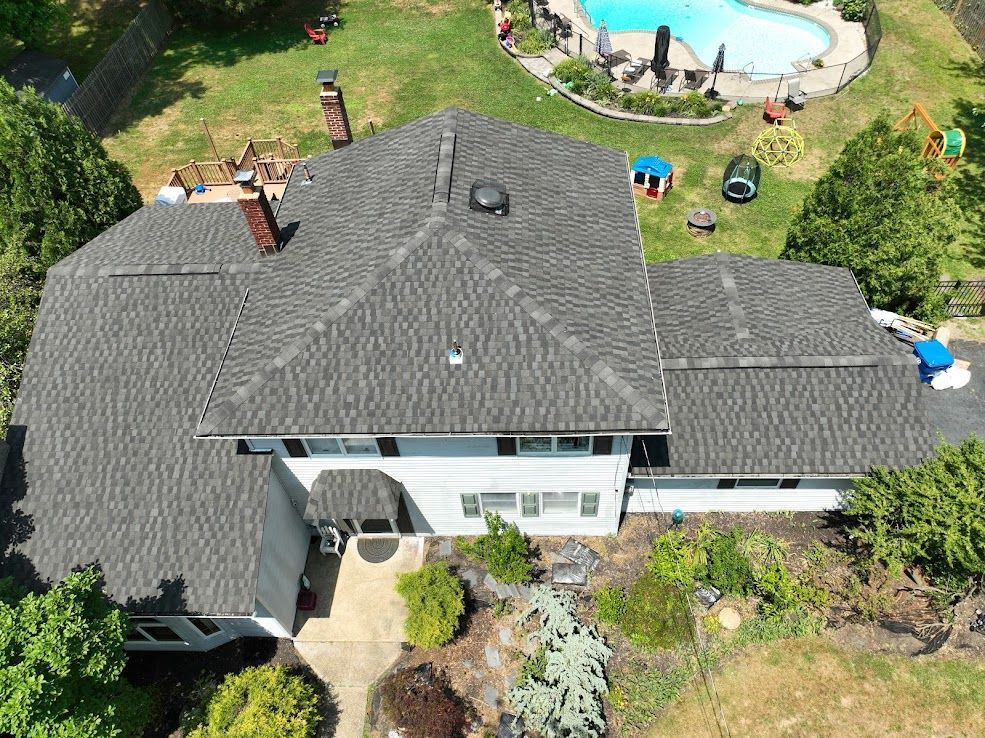 Aerial view of a gray-roofed house with a swimming pool and yard.