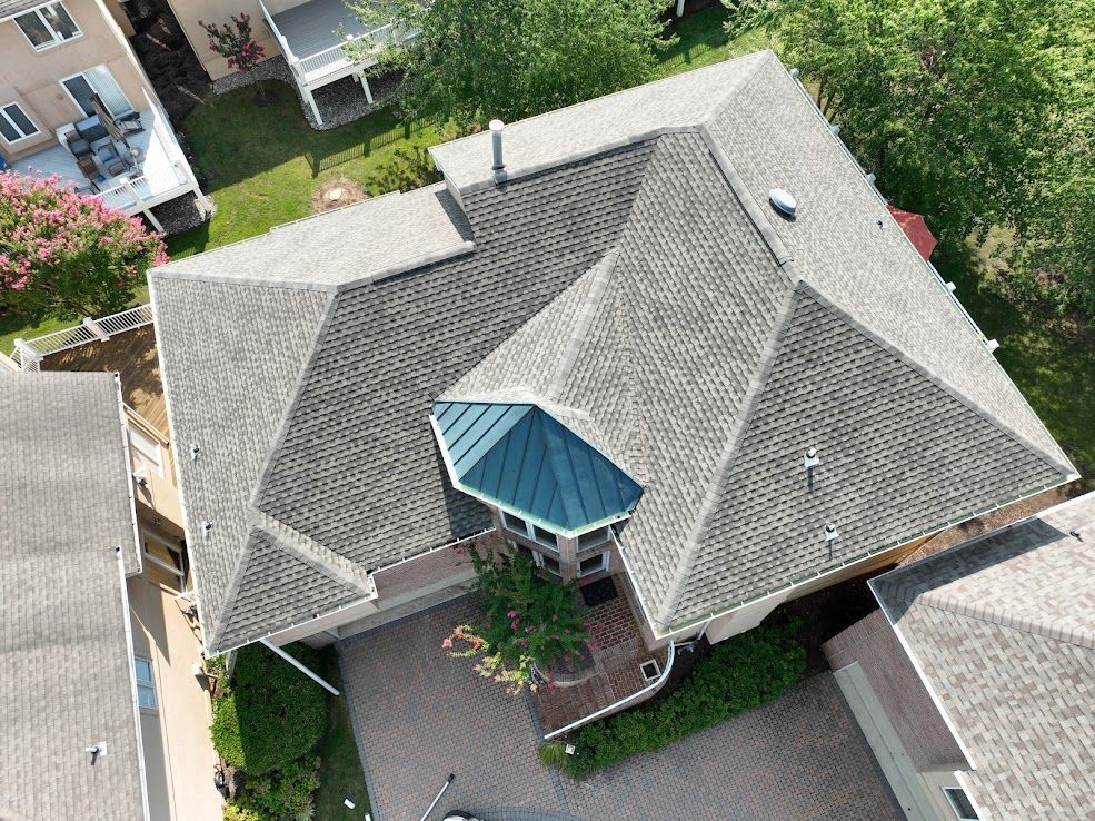 Overhead view of a house with a complex gray shingle roof and a teal-roofed entry section.