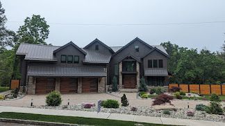 Gray-sided house with wooden garage doors and a well-manicured yard. Overcast sky.