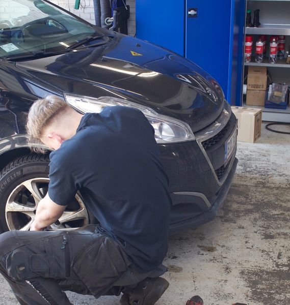 Mekaniker skifter dæk på en sort bil i en garage.