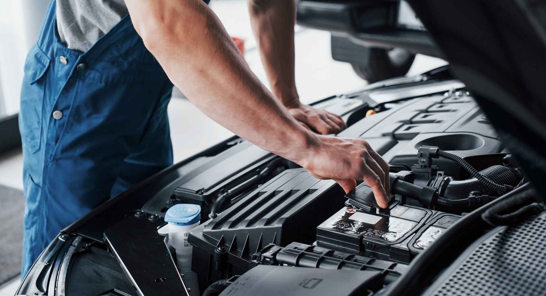 Mekaniker i blå overalls undersøger en bilmotor og holder styr på komponenterne i en garage.