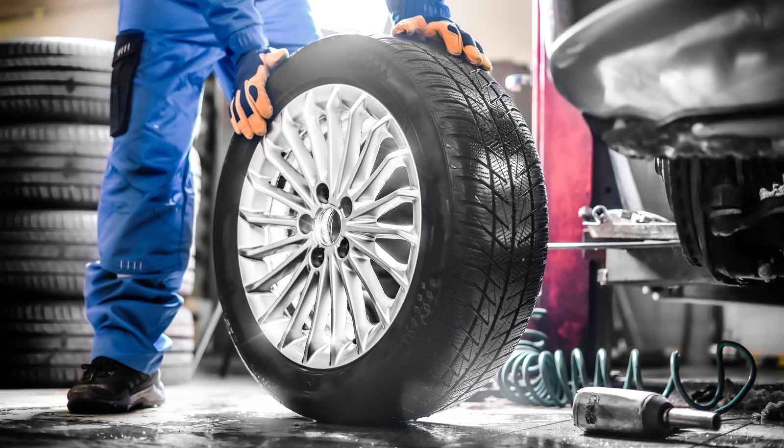 Mekaniker i blå overalls holder et bildæk med sølvfælg i autoværksted.